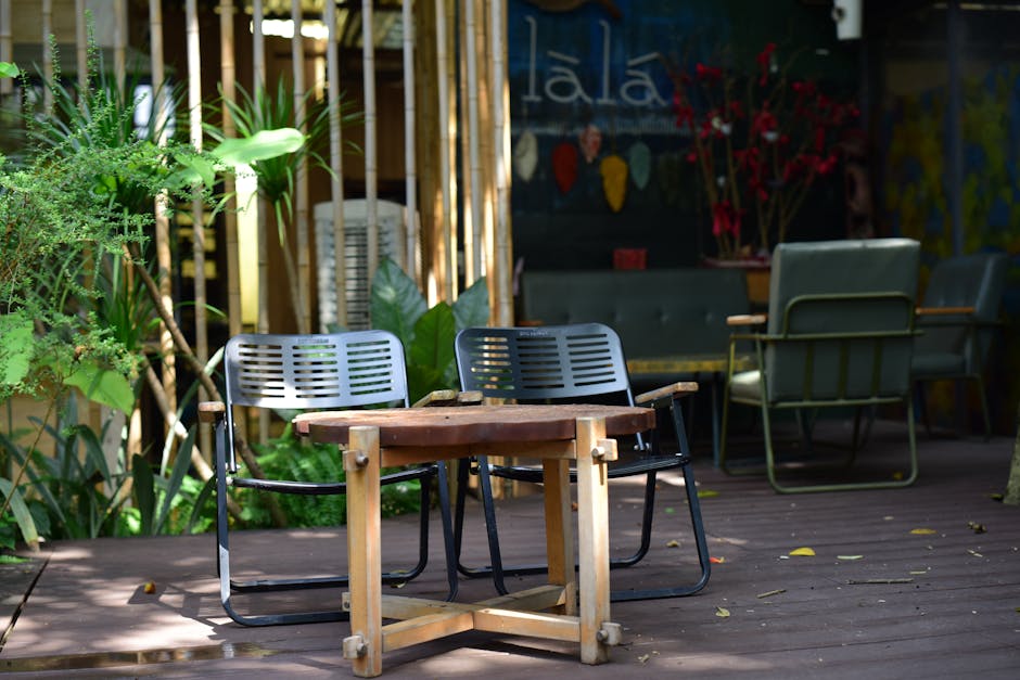 An inviting outdoor cafe setting with empty chairs and wooden table surrounded by lush plants.
